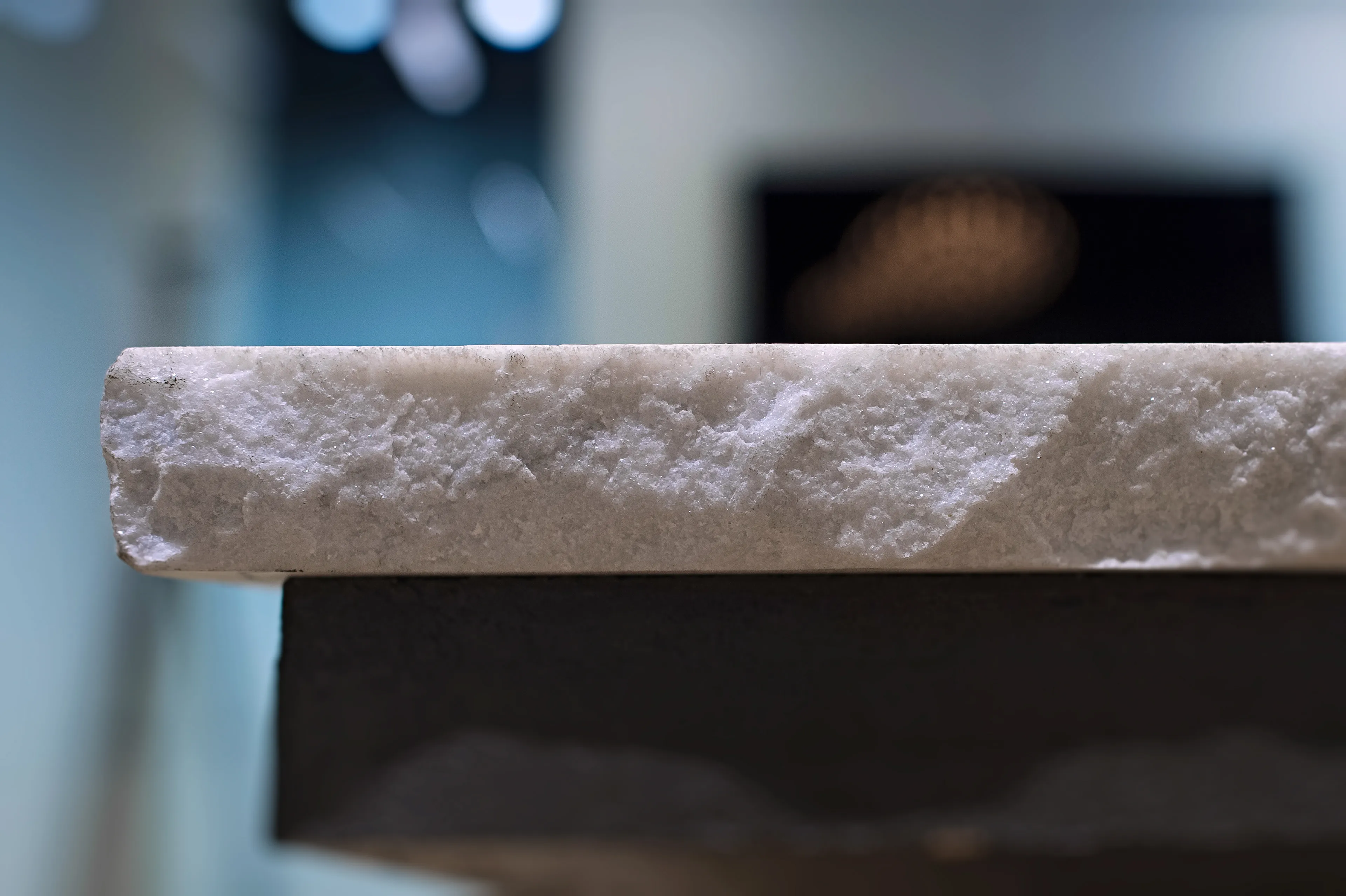 Close view of the marble table's rough edge, with the room softly out of focus behind it